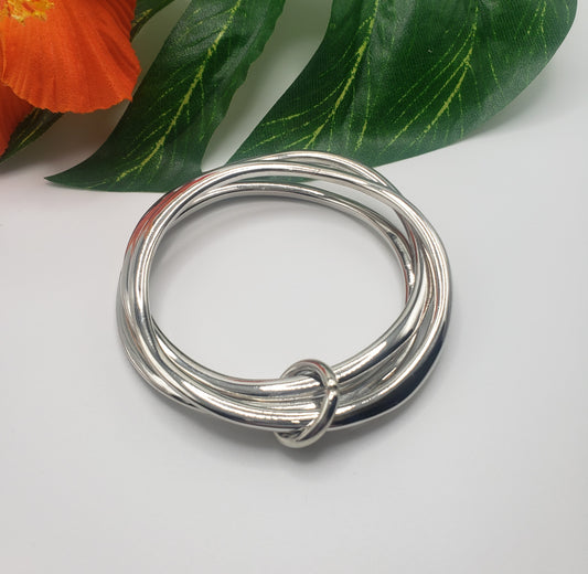 Tubular bangle bracelet set in silver displayed on a white surface with a green leaf and orange flower in the background from Fashion Go.