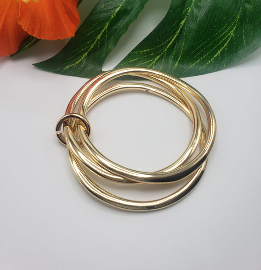 Fashion Go's TUBULAR BANGLE SET GOLD on a white surface with green leaves and an orange flower in the background.