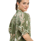 A woman wearing the Umgee Floral Print Puff Sleeve Top in olive green with pearl earrings, glancing over her shoulder against a white background.
