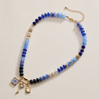 Introducing the Textured Glass Bead Necklace with Charm Trio by Lilla Haven—a stunning blue-toned piece adorned with gold-toned spacers and accents. This necklace features delightful charms, including a lock, key, flower, and pearls, all finished with an adjustable gold chain clasp for the perfect fit. Effortlessly blending elegance and whimsy, this unique Lilla Haven design is a standout accessory for any occasion.