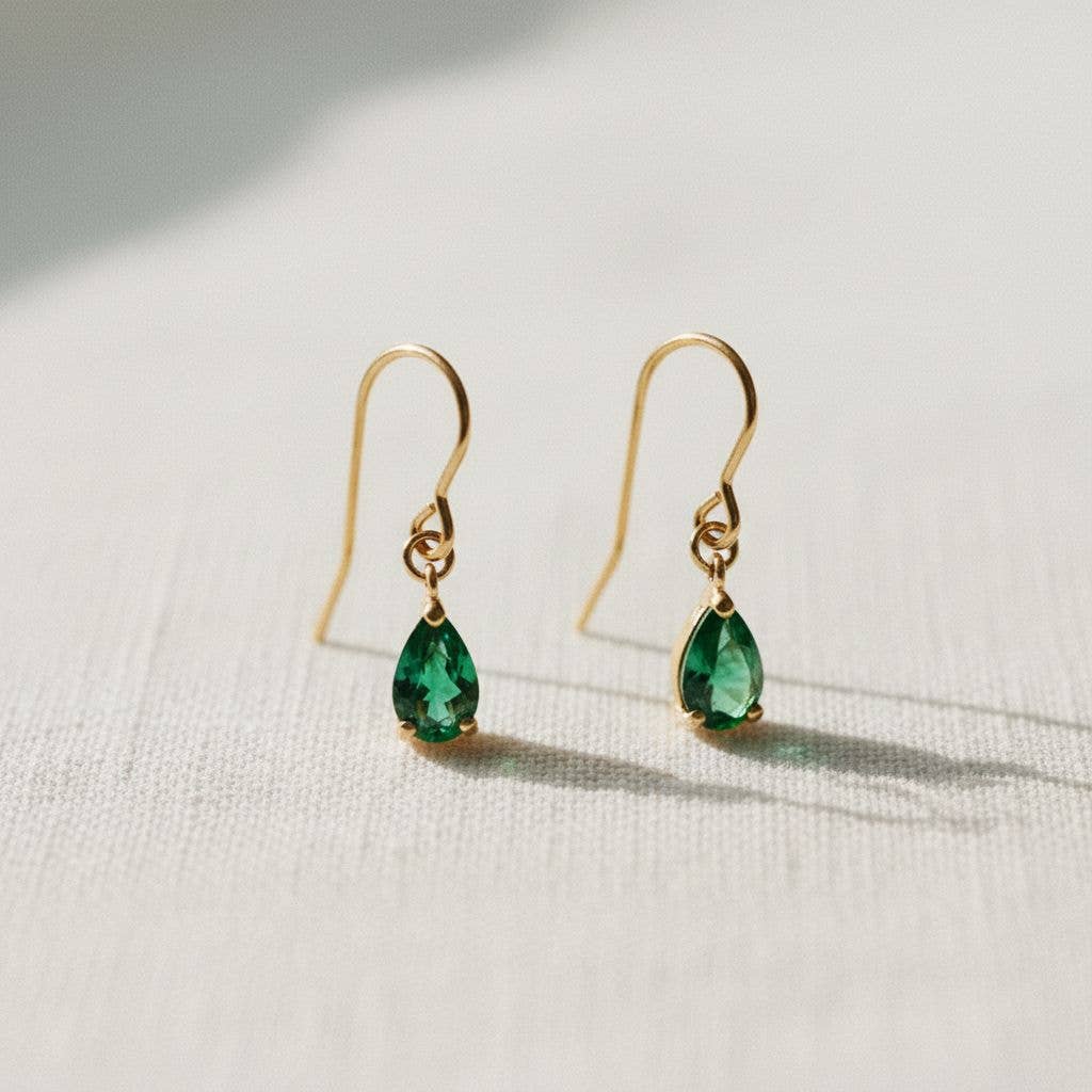 A pair of Ellemadera Chic Gemstone Dangle Earrings featuring green teardrop-shaped gemstones and gold hooks, displayed on a light-colored textured surface.