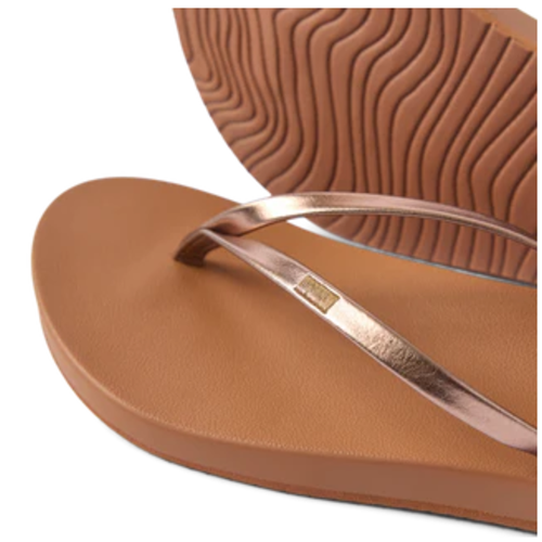 A close-up of the REEF Cushion Slim Flip Flop, featuring brown cushioned soles with textured grip and metallic rose gold straps accented by a subtle bronze shimmer. Main image