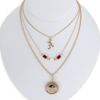 The Alabama Gold & Tube Bead Trio Necklace Set by Seasons Jewelry is showcased on a white bust, featuring three layered gold necklaces: one with an "A" pendant, another adorned with crimson tube beads inspired by Bama jewelry, and a third with a round, detailed charm for a sophisticated collegiate look.