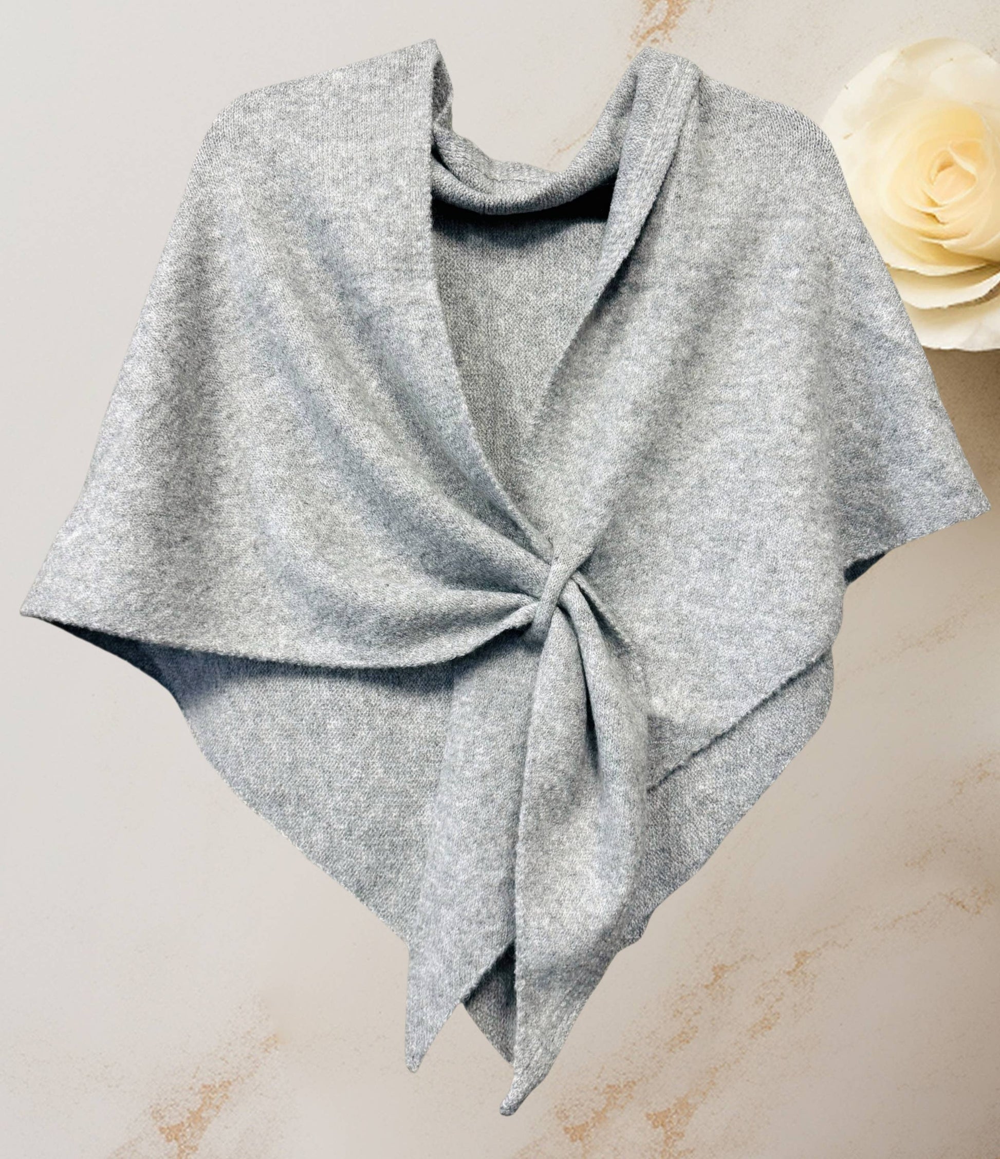 The JC Sunny Fashion Cashmere-Blend Knit Triangle Shawl features a chic cross-front design in light gray, displayed on a neutral background with a cream rose in the upper right corner.