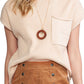 A person is wearing Shewin's Patch Pocket Ribbed Knit Short Sleeve Sweater in beige, paired with a wooden circle necklace and a brown buttoned skirt, ideal for transitional weather.