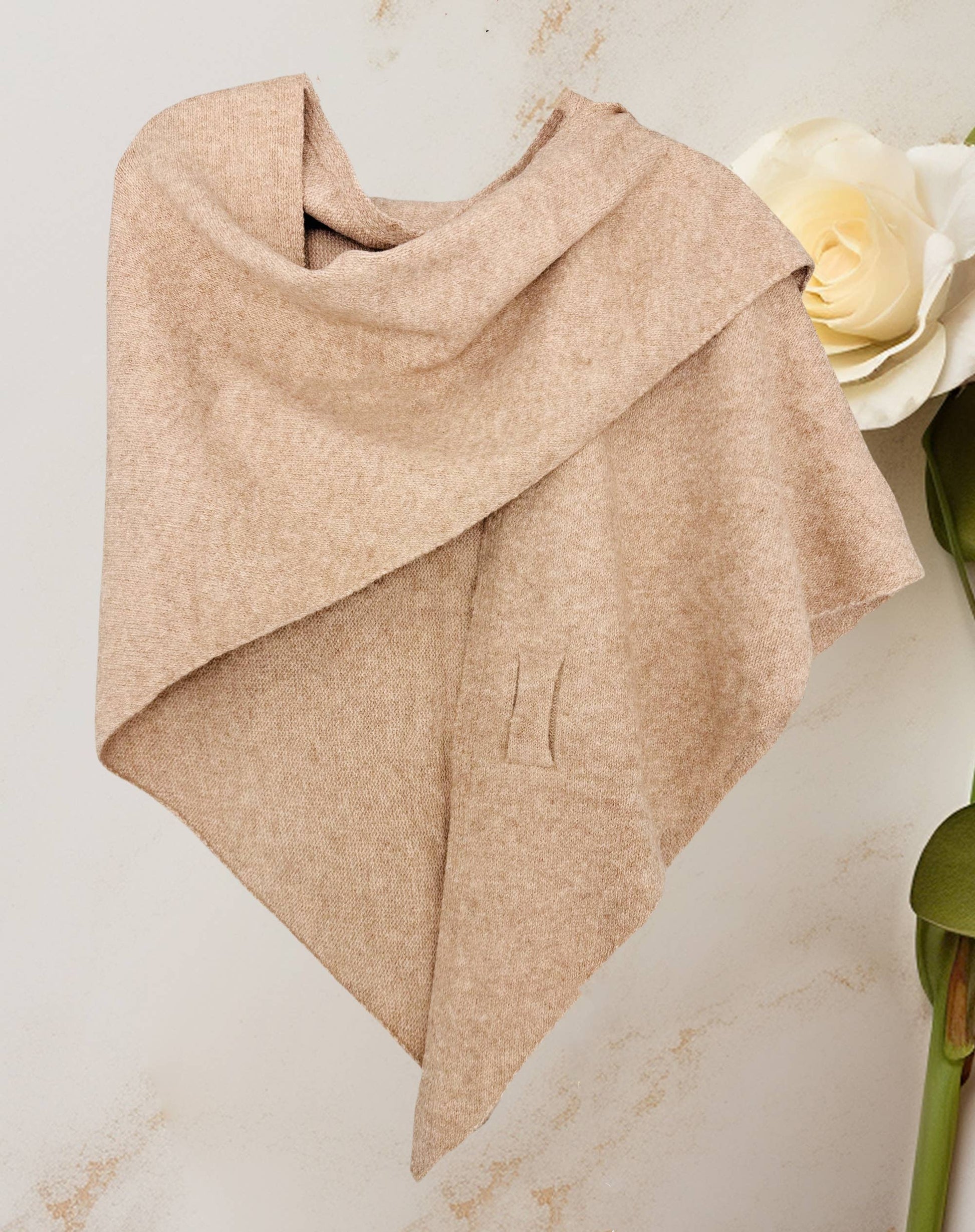 The JC Sunny Fashion Cashmere-Blend Knit Triangle Shawl with a cross-front design hangs on a light wall beside a white artificial flower.