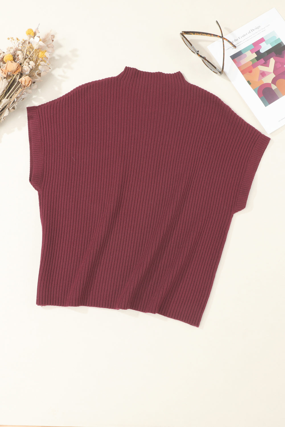 The Shewin Patch Pocket Ribbed Knit Short Sleeve Sweater in maroon, ideal for transitional weather, is arranged beside glasses, a book, and dried flowers on a light surface.