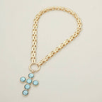 Sensibling Corp.’s Pearl Cross Charm Pendant Chunky Chain Statement Necklace is showcased on a light, neutral background. This gold chain necklace features a textured cross pendant adorned with six round blue gemstones.