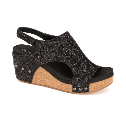 Introducing the Corkys Carley blk glitter from CORKY'S FOOTWEAR INC—a single black wedge sandal featuring a glittery upper, open toe, ankle strap with an adjustable closure, and a cork heel. Stud details enhance the look just above the cork sole.