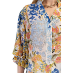Close-up of a person wearing the FASHION GO Floral Print Button Down Top with blue, yellow, and pink flowers and 3/4 sleeves, paired with a gold chain necklace. Only the upper torso and part of one arm are visible.