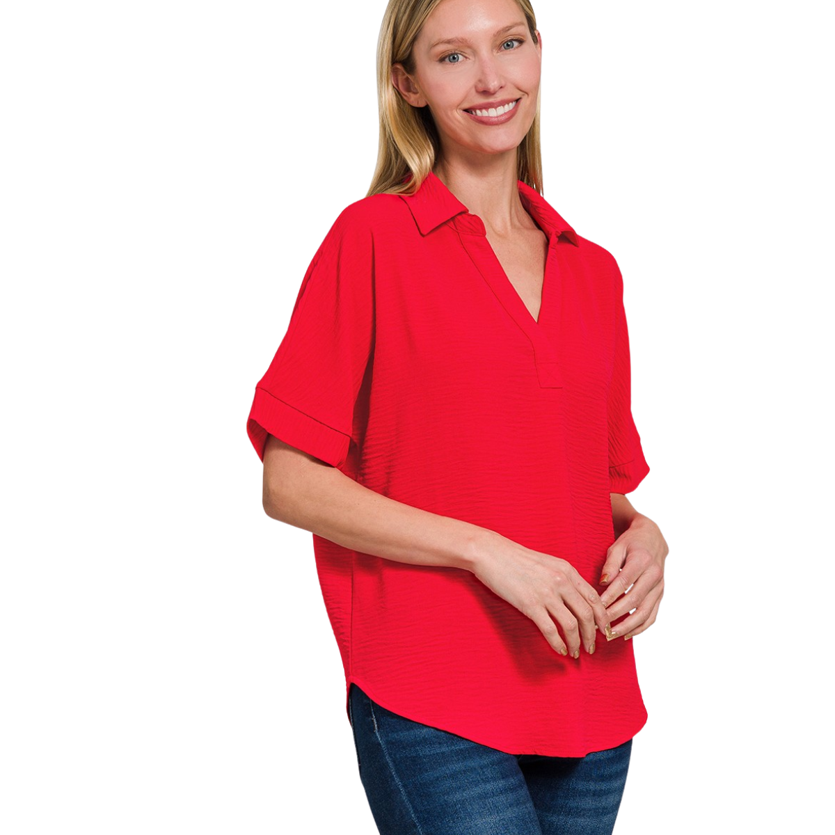 A woman stands smiling against a white background, wearing the Flipflops & Whatnots Woven Airflow Collared Top in red with short sleeves and blue jeans.