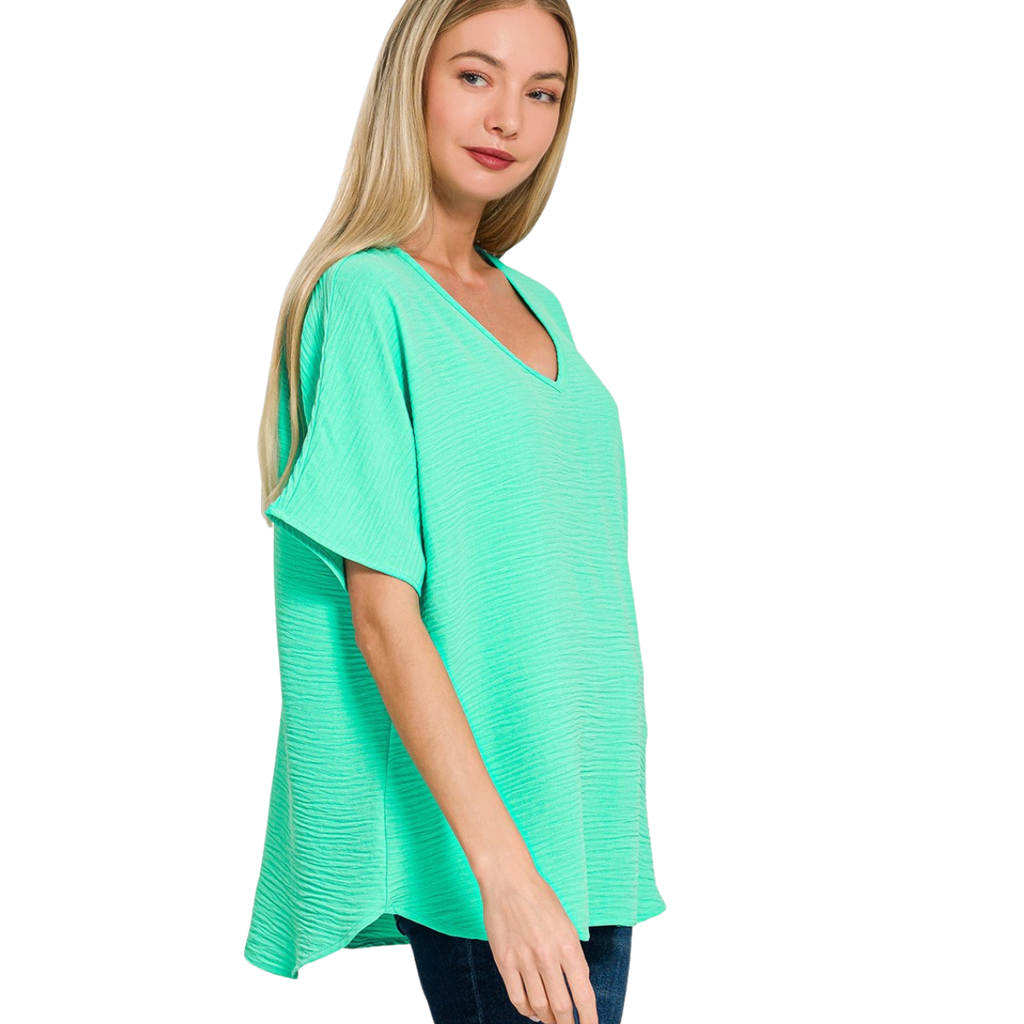 A woman wears the Zenana V-Neck Airflow Shirt Sleeve Top in mint green with dark jeans, standing against a white background.