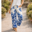A person wears Pine Apparel’s Pull On Border Print Pant with blue floral designs and a white sleeveless top, walking outdoors on a stone path lined with potted plants.