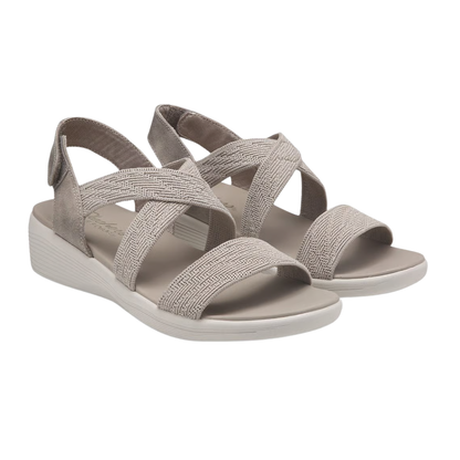A pair of SKECHERS Arya Very Midful Low Wedge Heel Sandals in light beige, featuring open toes and crisscross elastic straps, is displayed on a white background.