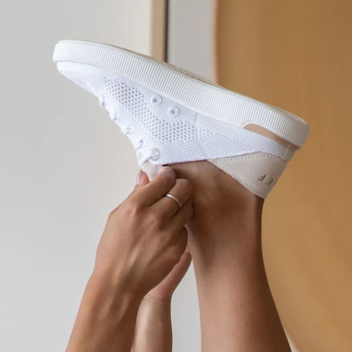 A person holds up the REEF Reef Neptune Sneaker, highlighting its lightweight knit texture, crushable heel, and memory foam insole in a sleek white design.