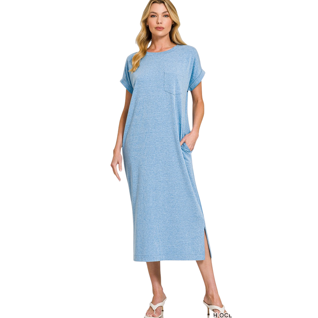 A woman stands against a white background wearing the Zenana Round Neck Short Sleeve Midi T-Shirt Dress in light blue, featuring a cotton blend fabric, side pockets, chest pocket, short sleeves, and round neckline.