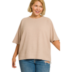 A woman smiles against a white background, wearing the Zenana Double Knit Short Sleeve Top in beige with ripped blue jeans—an effortless everyday look.