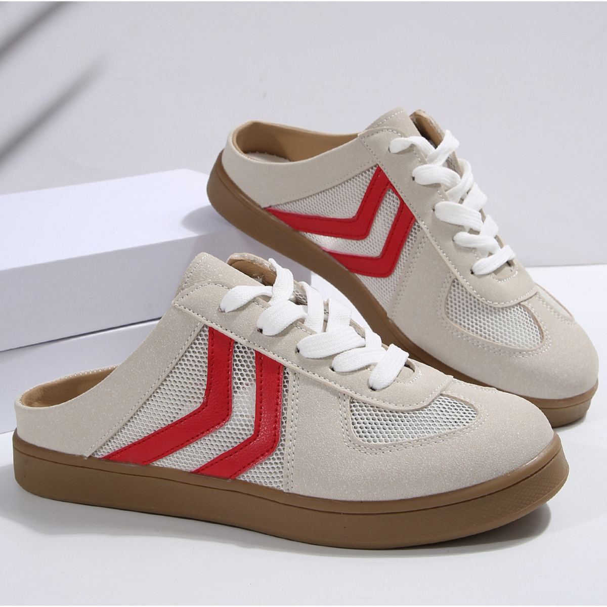 The Mesh Low Back Slip On Sneakers by FASHION GO feature a beige slip-on design with white laces, breathable mesh panels, red chevron stripes on the sides, and brown rubber soles. Displayed against a white background, they offer a stylish athletic look.