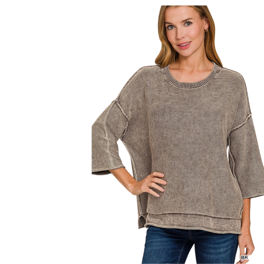 A woman wears a Women’s Washed Cotton Boxy Sweater with 3/4 Sleeves in taupe, featuring a boxy silhouette and exposed seams, paired with blue jeans.