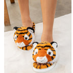 A person stands on a white rug wearing FASHION GO Tiger Fuzzy Slippers, which are plush and furry with tiger face designs, feature non-skid soles, and are available in women’s shoe sizes.
