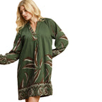 A woman wearing the Umgee Botanical Print Green Dress, featuring a loose fit, long balloon sleeves, and an abstract brown and white leaf pattern, stands against a white background.