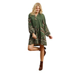 A woman wearing the Umgee Botanical Print Green Dress, featuring long balloon sleeves, stands on one leg in brown ankle boots against a white background.