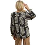 A person with long blonde hair, seen from behind, wears the Umgee Boho Paisley Blouse and tan pants, holding one hand to their head.