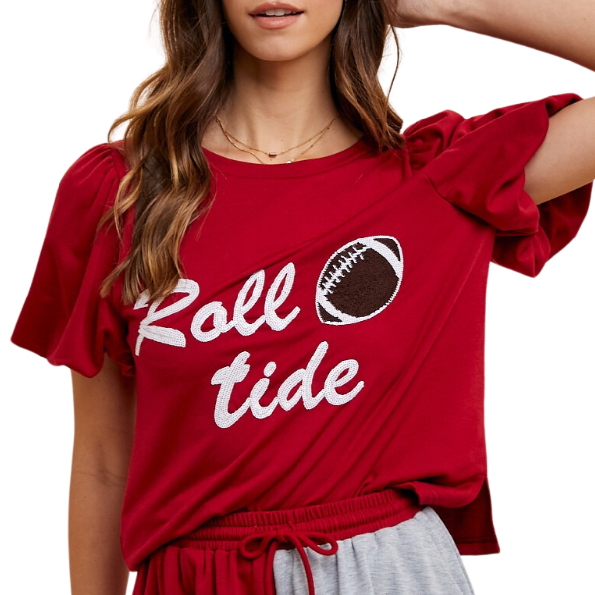 A person in a red team shirt with the text "Roll Tide" in sequin letters and an image of a football on the front. The person has long brown hair and wears matching red and gray athletic shorts, wearing the Roll Tide Top by FASHION GO.