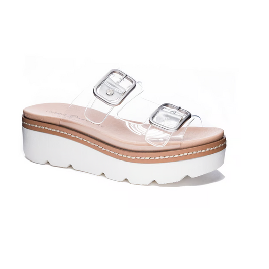 The Surf's Up Clear Wedge by Chinese Laundry features a tan footbed, a stylish platform sole, and two transparent straps with oversized buckles, all set against a white background.
