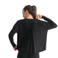 A woman with a ponytail is seen from the back wearing the Mono B Brushed Hacci Long Sleeve Top in black, relaxed fit, gently holding the neckline with one hand.