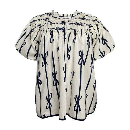 The Umgee Off White and Navy Ribbons and Bows Top is a short-sleeve, white boxy fit blouse with a gathered neckline and puff sleeves, featuring a ribbon print pattern of navy blue bows.