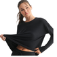 A woman wearing the Mono B Brushed Hacci Long Sleeve Top holds out the bottom of her black shirt, showing part of her midriff.