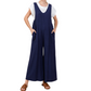 Person wearing a white t-shirt under a comfy Jumpsuit by Jodifl featuring sleeveless, wide-leg blue pants with hands in pockets; brown slip-on sandals are visible. The stylish attire offers the perfect blend of relaxation and chic fashion.