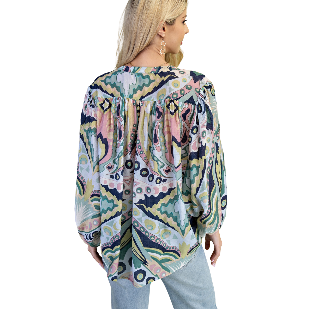A woman with long blonde hair, facing away, wears the FASHION GO Printed Loose Fit Button Down Blouse with green, pink, blue, and beige designs, paired with light blue jeans. The blouse is long-sleeve and has a relaxed fit.
