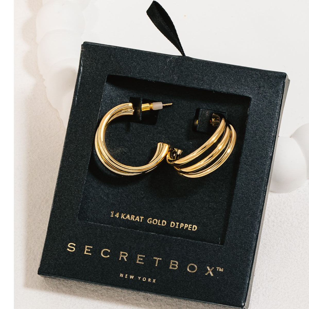 A pair of Secret Box Gold Dipped Layered Tube Hoop Earrings in Gold, 14 karat gold dipped hoop earrings rests inside a sleek black box adorned with the brand name "FASHION GO. Main image