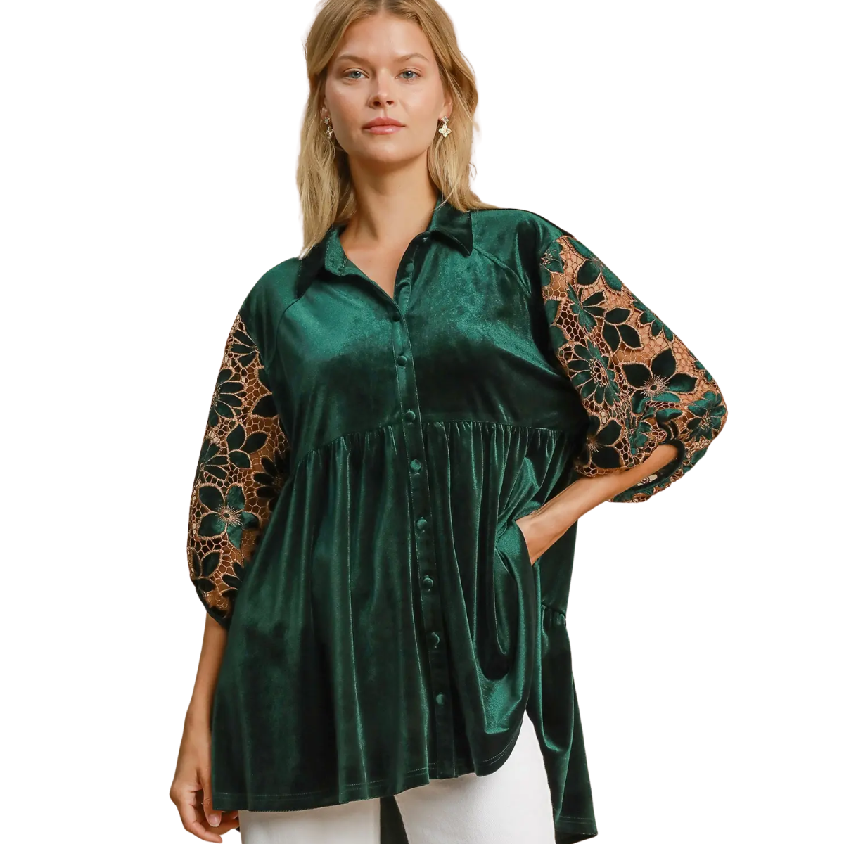 A woman models the Umgee Floral Lace Contrast Velvet Tunic, featuring green velvet with floral lace sleeves and puff details, styled with white pants against a plain background.