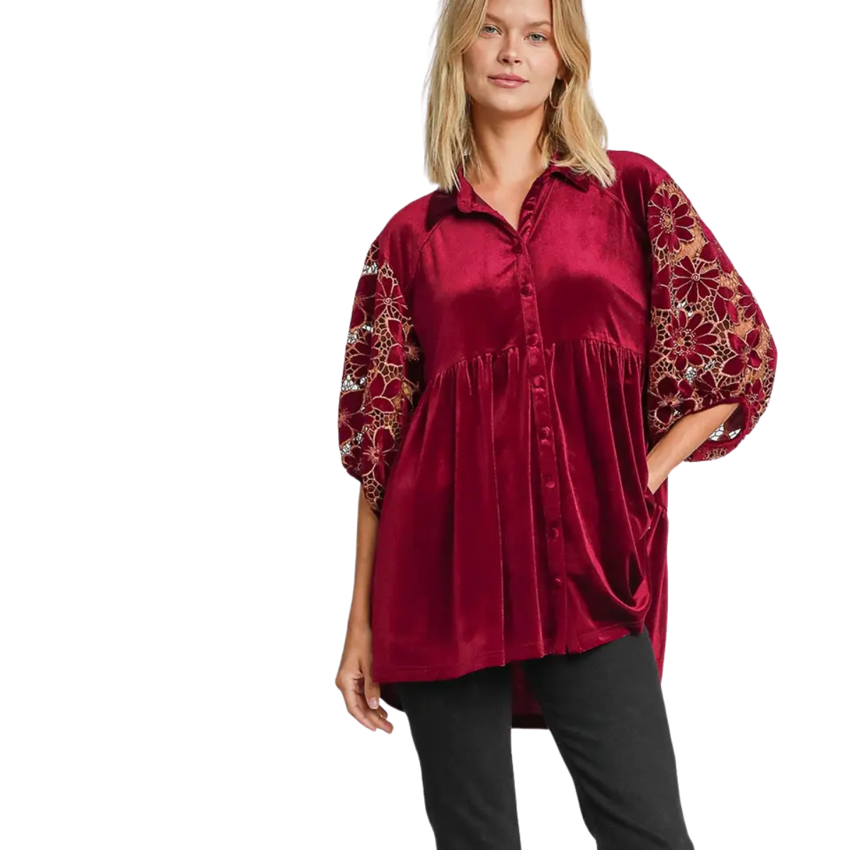 A woman models the Umgee Floral Lace Contrast Velvet Tunic—a loose-fitting red velvet top with floral lace sleeves—paired with black pants, standing against a white background.