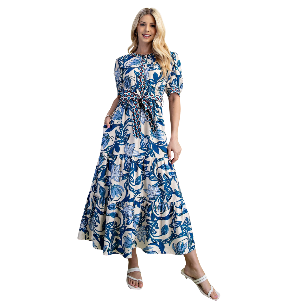A woman wears the FASHION GO Colbalt Mix Pattern Tie Waisted Dress—long, blue and white floral print with short sleeves and a waist tie—and white sandals, smiling against a white background. Main image