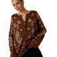 A woman wears the FASHION GO Brown and White Paisley Pattern Cardigan, featuring cozy knit fabric with paisley and geometric designs, buttoned up against a plain white background.