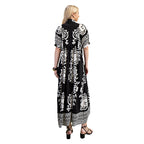 A woman stands with her back to the camera, wearing the FASHION GO Deserving Black and White Print Dress featuring a smocked yoke and bold mixed print patterns, paired with black sandals, earrings, and a bracelet, set against a white background.