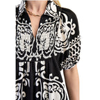 A person wearing the Deserving Black and White Print Dress by FASHION GO, featuring white floral patterns, a deep V-neck, puffed sleeves, and accessorized with a gold chain necklace.