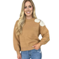 A woman wears the Carole Christian Bow Shoulder Sweater in Camel, featuring an ivory flower bow accent on the left shoulder, paired with blue jeans against a white background.