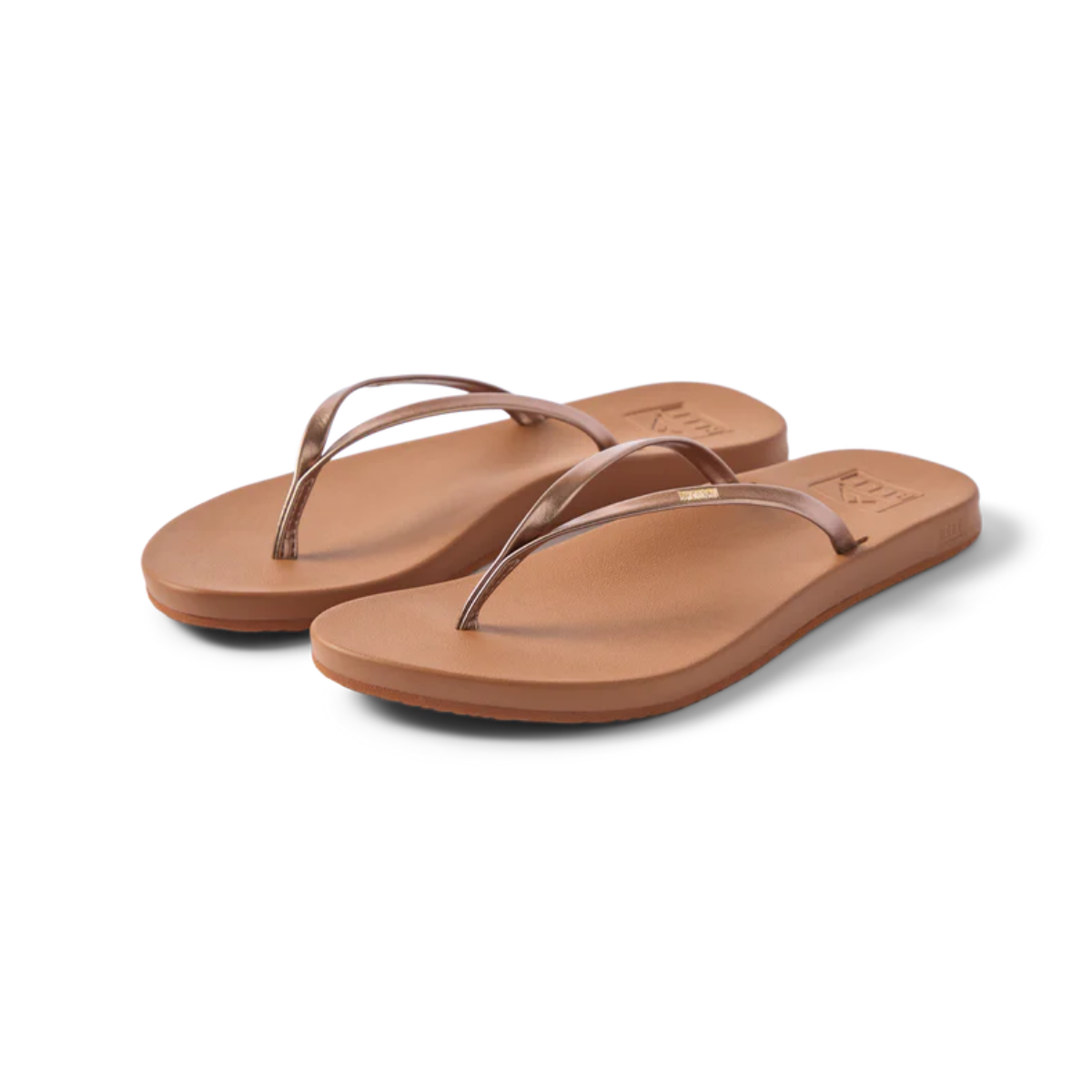 The REEF Cushion Slim Flip Flop in Bronze features thin metallic straps and flat soles in a brown hue, displayed on a plain white background.