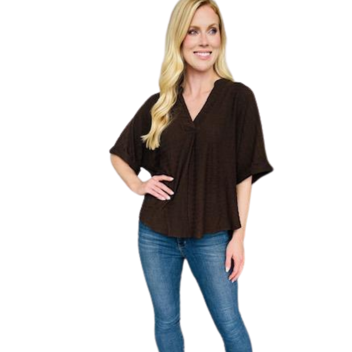 A woman with long blonde hair smiles, standing with one hand on her hip, wearing a Carole Christian Oversized Chocolate Short Sleeve Blouse and blue jeans.