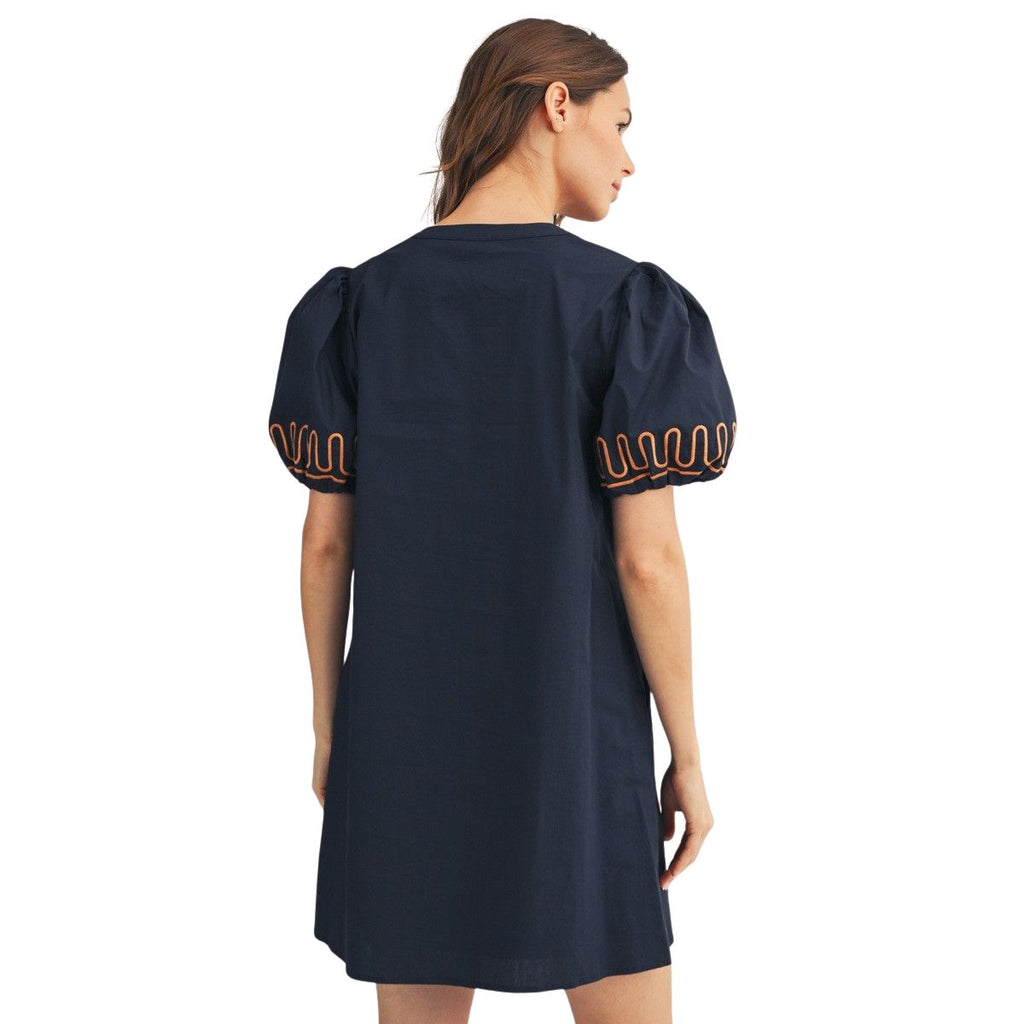 A woman stands facing away, wearing the FASHION GO Short Puff Sleeves Embroidered Shift Dress in navy blue cotton, which features orange embroidered details.