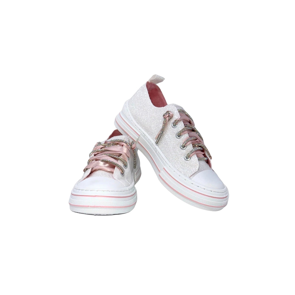 The Aman Mary’s Version White Glitter Sneakers by VERY G, featuring pink accents, rhinestone laces, and pink details, are displayed against a white background.