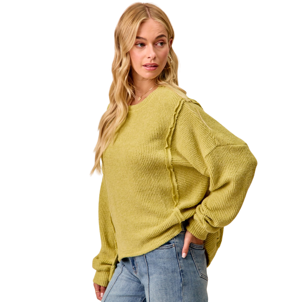 A woman wears the FASHION GO Boucle Rib Knit Uneven Hem Top in yellow-green with blue jeans, standing with one hand in her pocket and looking to the side.