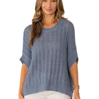 A woman wears the Sew In Love Relaxed Fit Dolman Sleeves Open Knit Top in blue with white pants, standing against a white background.