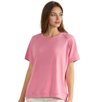 A woman stands against a plain white background, facing slightly to the side, wearing the FASHION GO Everyday Soft Ribbed Loose Fit Short Sleeve Top in pink paired with white pants.