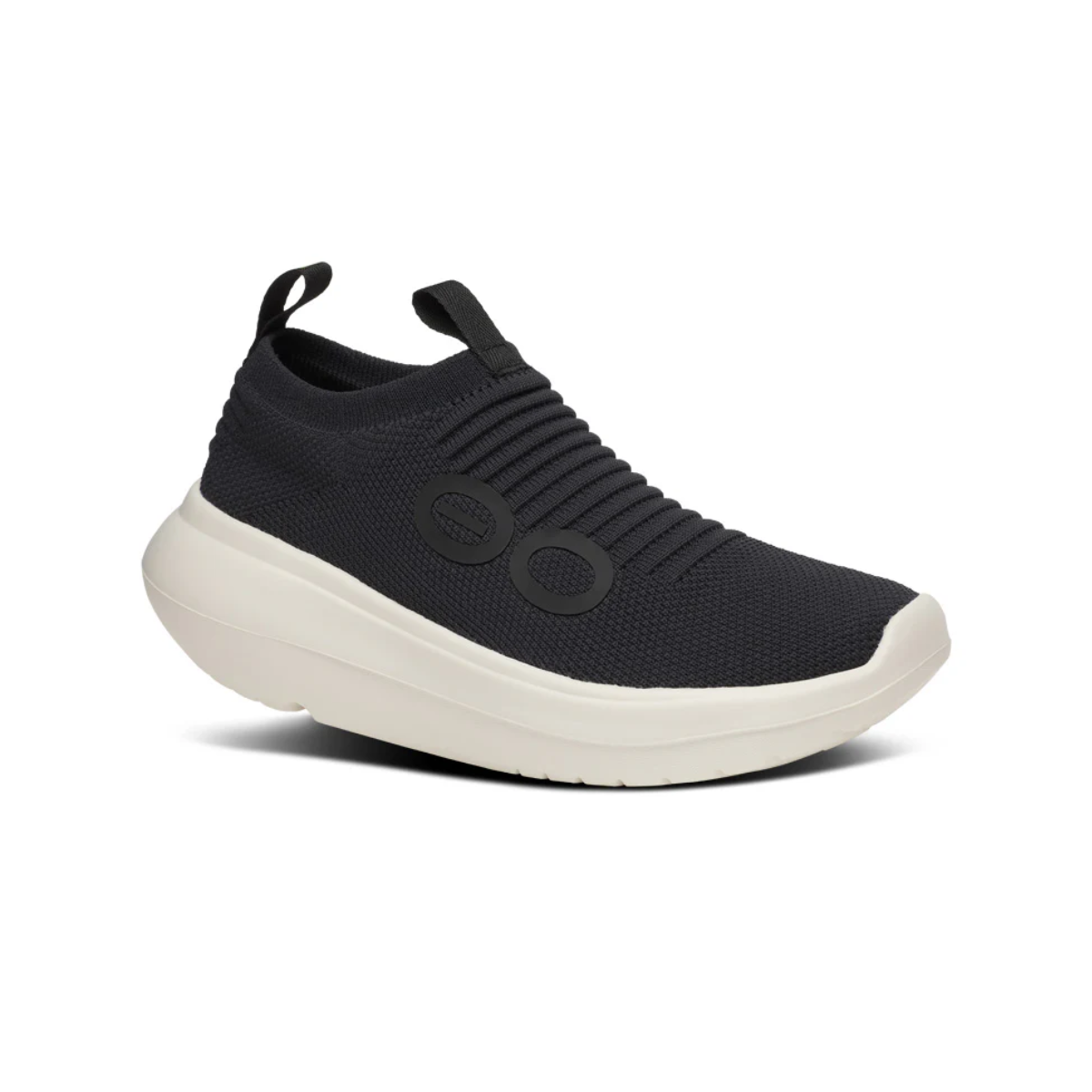 The OO My Zen in Black by OOFOS LLC is a black slip-on recovery shoe featuring a ribbed knit upper, two circular side patterns, and a thick white sole.